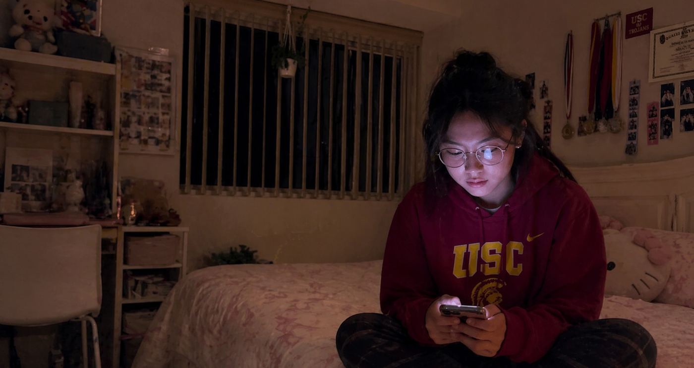 Alicia on her bed, her face lit by her phone.