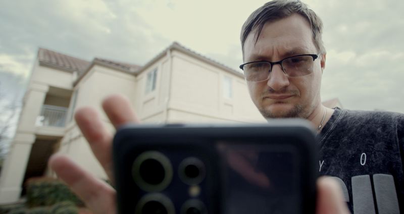 Dalton looks down at his phone outside a house.