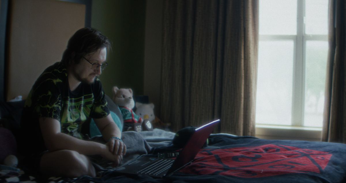 Dalton sits on his bed in a dim room, looking at his laptop.
