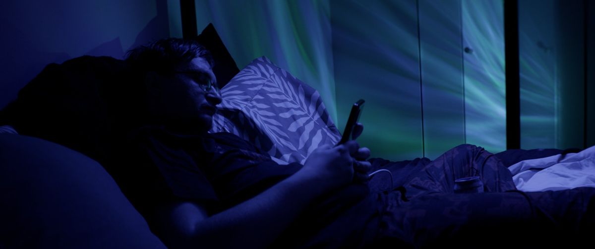 Dalton lies in bed in blue light, looking at his phone.
