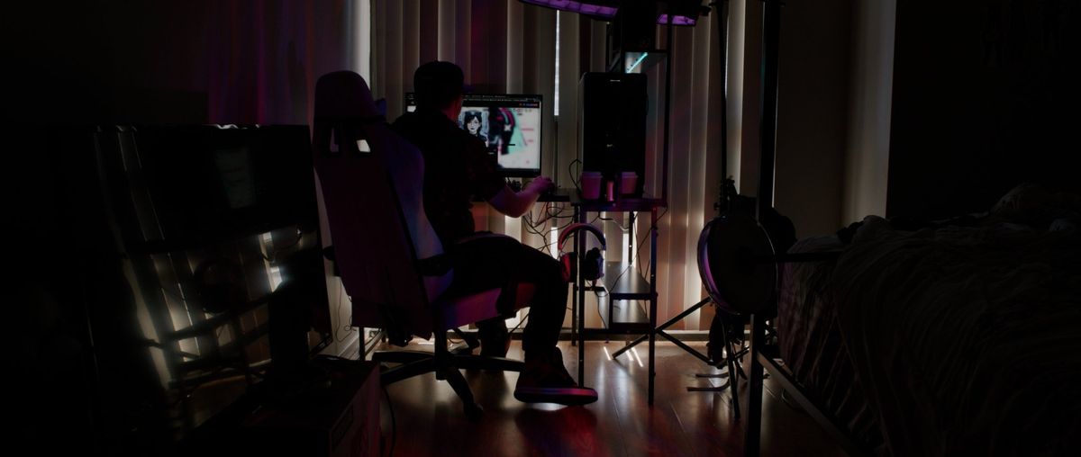 Dalton at his desk at night, with Xia's face on the monitor.